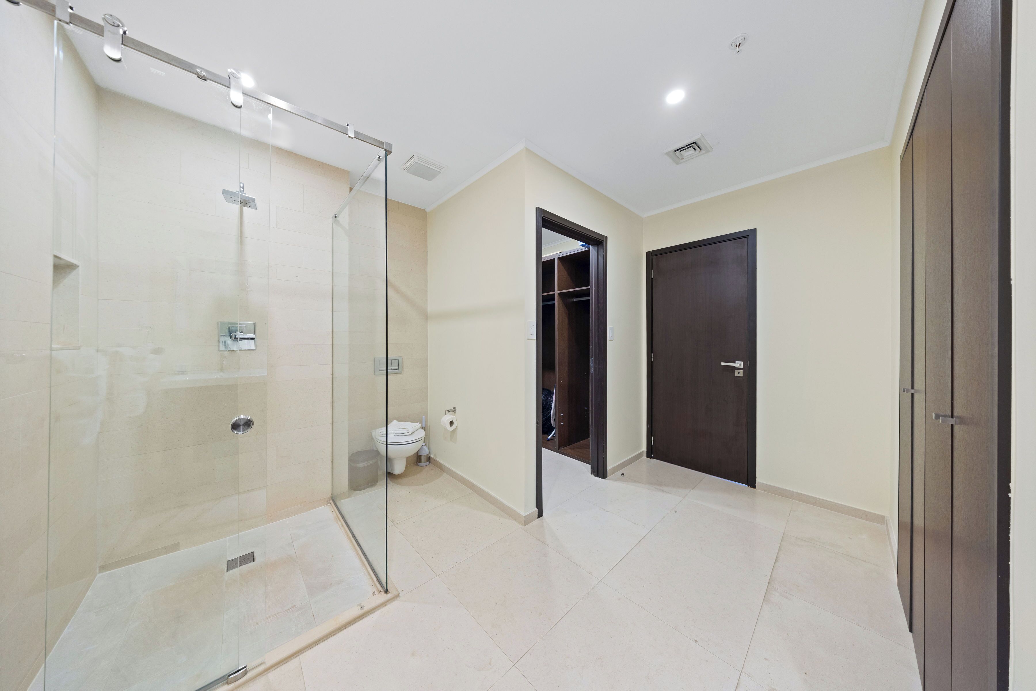 A modern bathroom with a glass-enclosed shower, a toilet, and a dark wooden door.