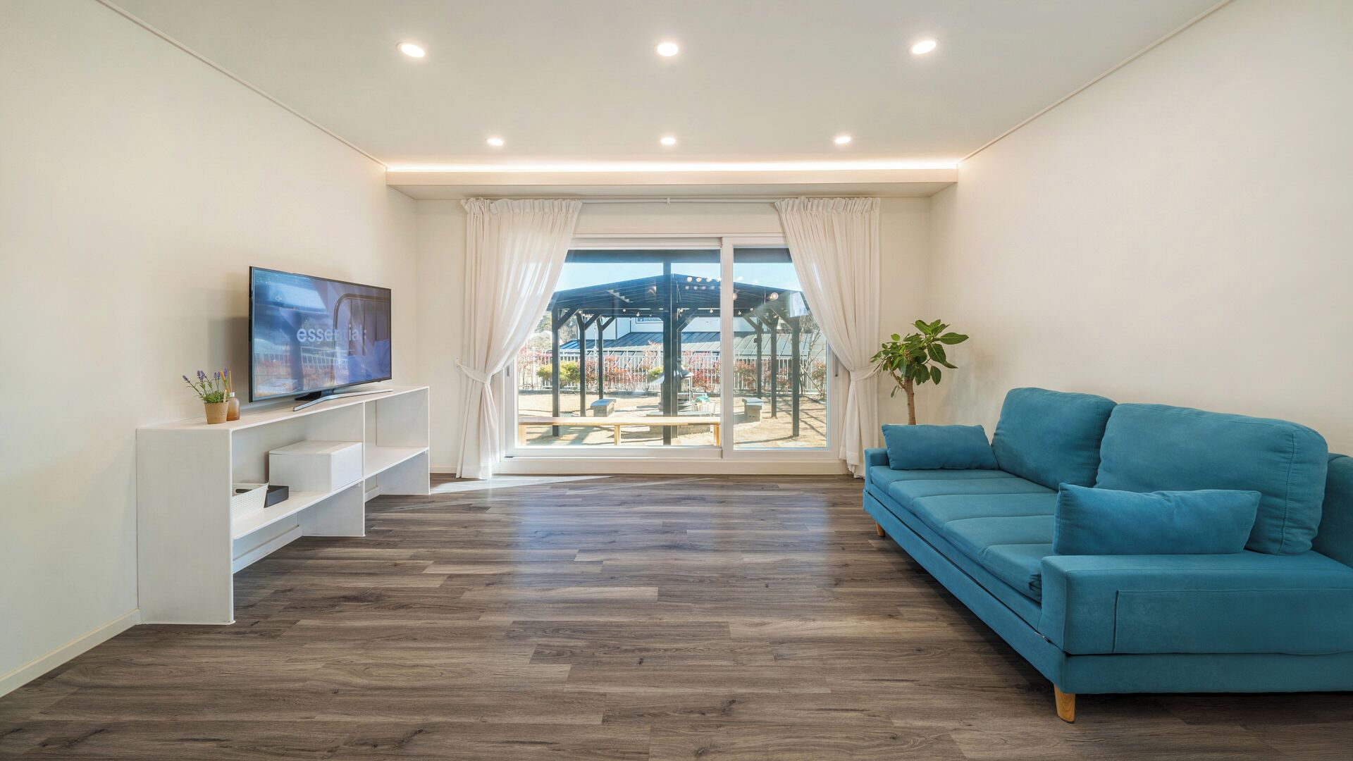 A modern living room with a flat-screen TV, a blue sofa, and a wooden floor.