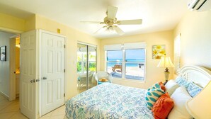 Une chambre avec un lit, un ventilateur de plafond, une fenêtre donnant sur la plage et une porte menant à une autre pièce.