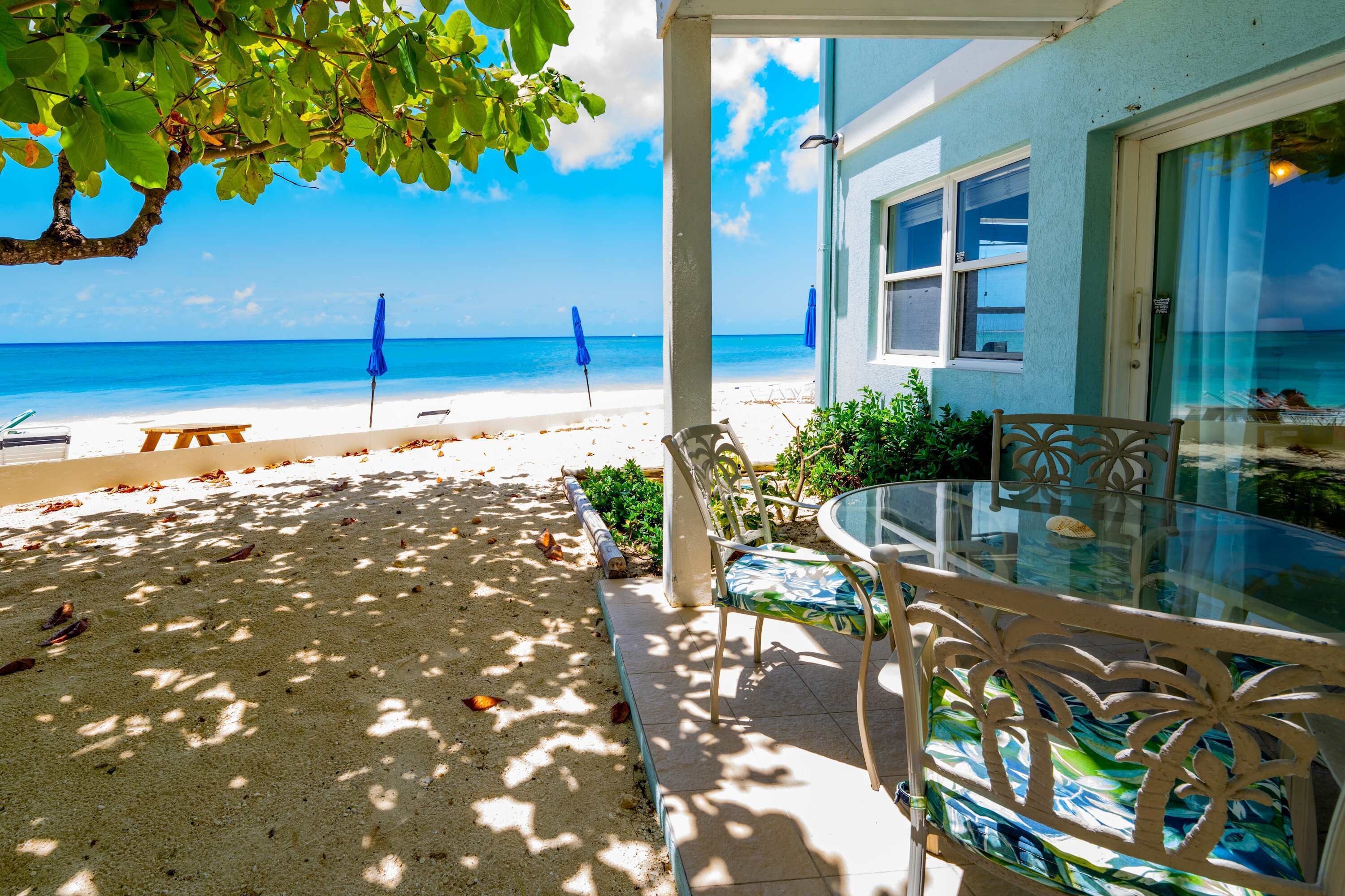 Eine Terrasse am Strand mit einem Glastisch und Stühlen, Blick auf den Ozean und eine überdachte Sitzgelegenheit mit Sonnenschirmen.