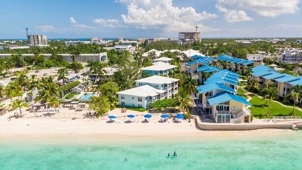Un hôtel situé en bord de mer, composé de plusieurs bâtiments aux toits bleus, avec une plage de sable fin et une eau turquoise cristalline.