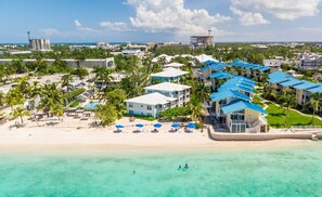 A beachfront hotel with multiple blue-roofed buildings, a sandy beach, and clear turquoise waters. - Beachfront Bliss - Seagull 1 Bdr Seven Mile Beach (West Bay)
