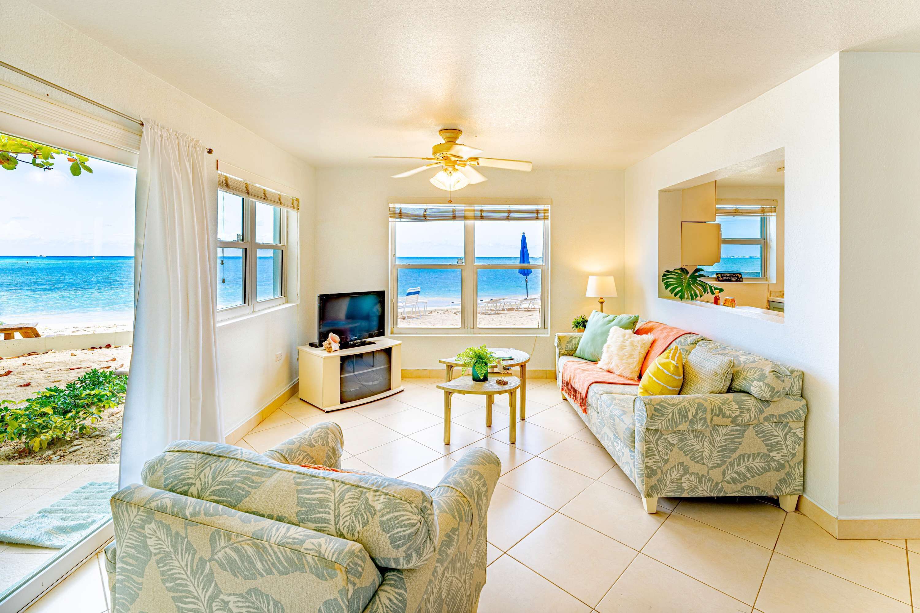 Ein Wohnzimmer mit Fernseher, Deckenventilator, Sofa, Couchtisch und Blick auf den Strand.