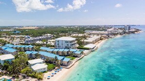 Une station balnéaire dotée de villas en bord de mer, d’une piscine et d’une plage aménagée avec des parasols.