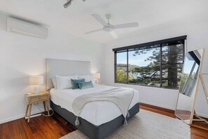 Une chambre à coucher avec un lit, une table de chevet, une lampe et une grande fenêtre donnant sur un beau paysage.