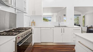 Cocina moderna con armarios blancos, estufa de acero inoxidable y ventana con vistas al exterior.