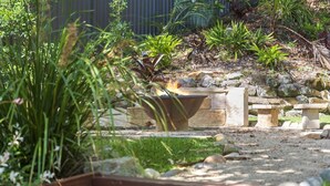 Un jardín con un pozo de fuego, bancos de piedra y diversas plantas.