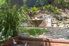 Ein Garten mit Feuerstelle, Stehbecken und verschiedenen Pflanzen.