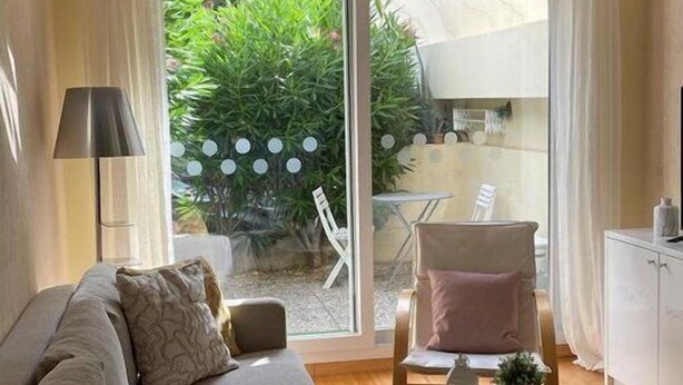 A modern living room with a sofa, a small round table, and a chair. There is a sliding glass door leading to a patio area with a table and chairs. - Delightful Studio With Private Parking, Beaulieu (Beaulieu-sur-Mer)