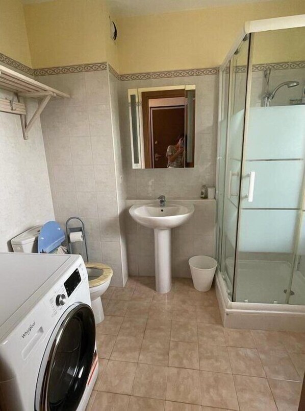 A compact bathroom with a washing machine, a sink, and a glass shower enclosure.