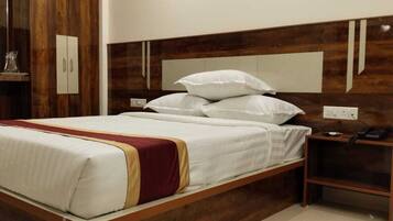A neatly made bed with white linens and a red and gold accent, a wooden headboard, and a bedside table with a phone and a lamp.