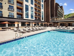 A hotel pool area with lounge chairs and umbrellas, a clear pool, and a building with multiple balconies.