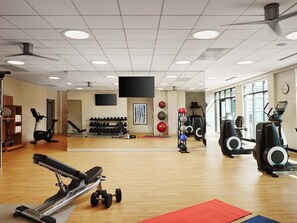 Un gimnasio con equipo de ejercicio, un espejo y una televisión instalada en la pared.