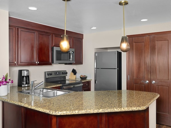 A kitchen with granite countertops, stainless steel appliances, wooden cabinets, and pendant lighting.