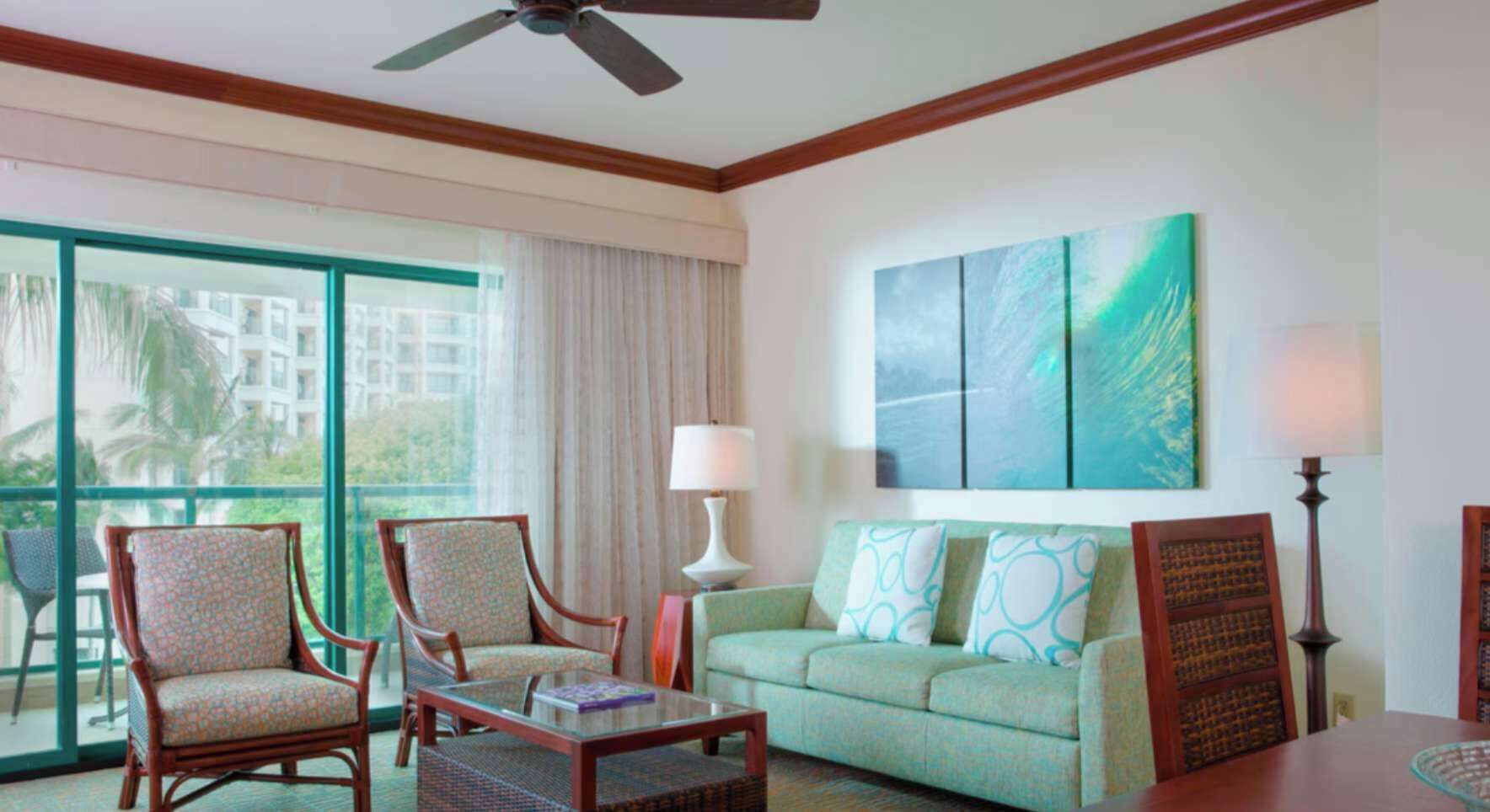 Habitación de hotel con balcón, sofá, dos sillones, una mesita de centro y un cuadro en la pared.
