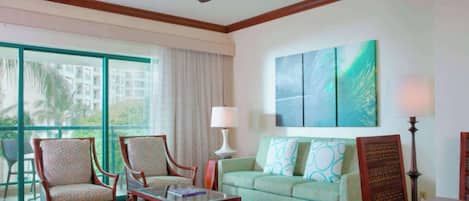 Habitación de hotel con balcón, sofá, dos sillones, una mesita de centro y un cuadro en la pared.