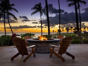 A fire pit with two Adirondack chairs facing a sunset over the ocean, surrounded by palm trees and greenery. - Marriott's Ko Olina Beach Club 1 BR OCEAN VIEW (Kapolei)