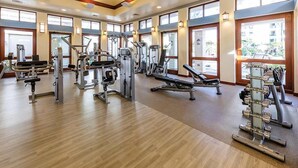 Ein Fitnessstudio mit verschiedenen Trainingsgeräten, großen Fenstern und Holzboden.