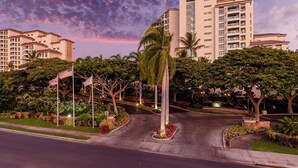 Ein mehrstöckiges Hotel mit begrüntem Eingangsbereich, Palmen und amerikanischen Flaggen.