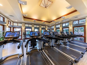 A gym with treadmills and exercise bikes, large windows, and a modern ceiling design.