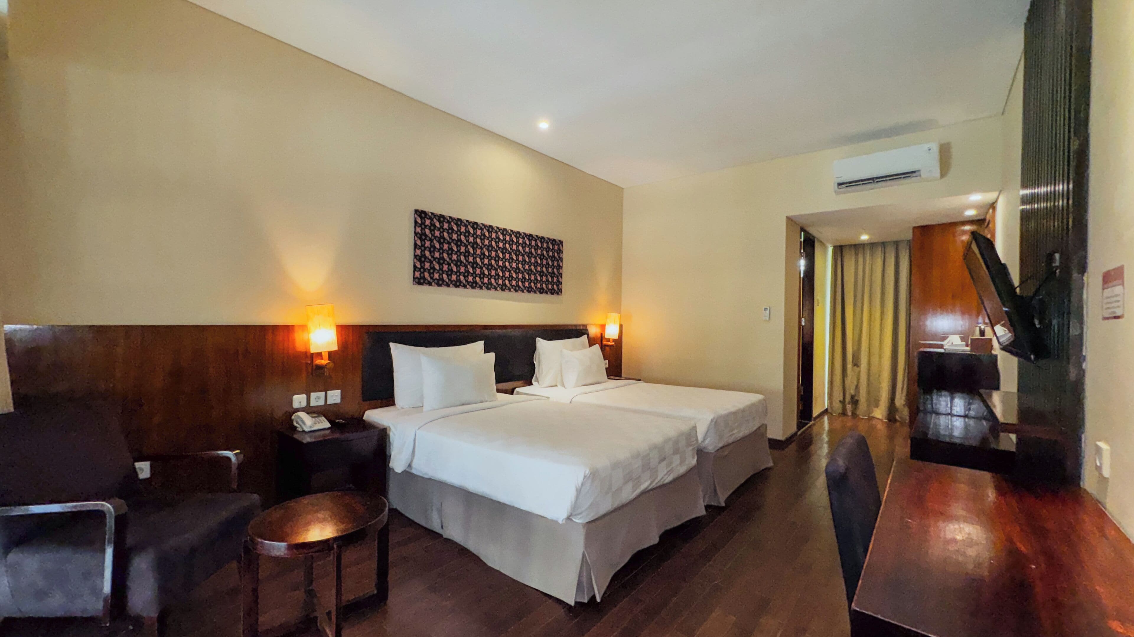 A hotel room with two beds, a desk, a chair, and a small table.