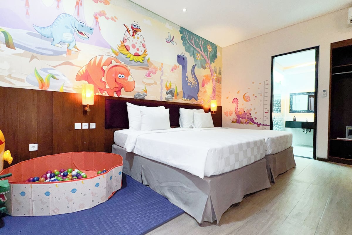 Ein Hotelzimmer mit einem großen Bett, einem Wandbild, einer kleinen Spielecke und einem durchgegangenen Tür sichtbaren Badezimmer.