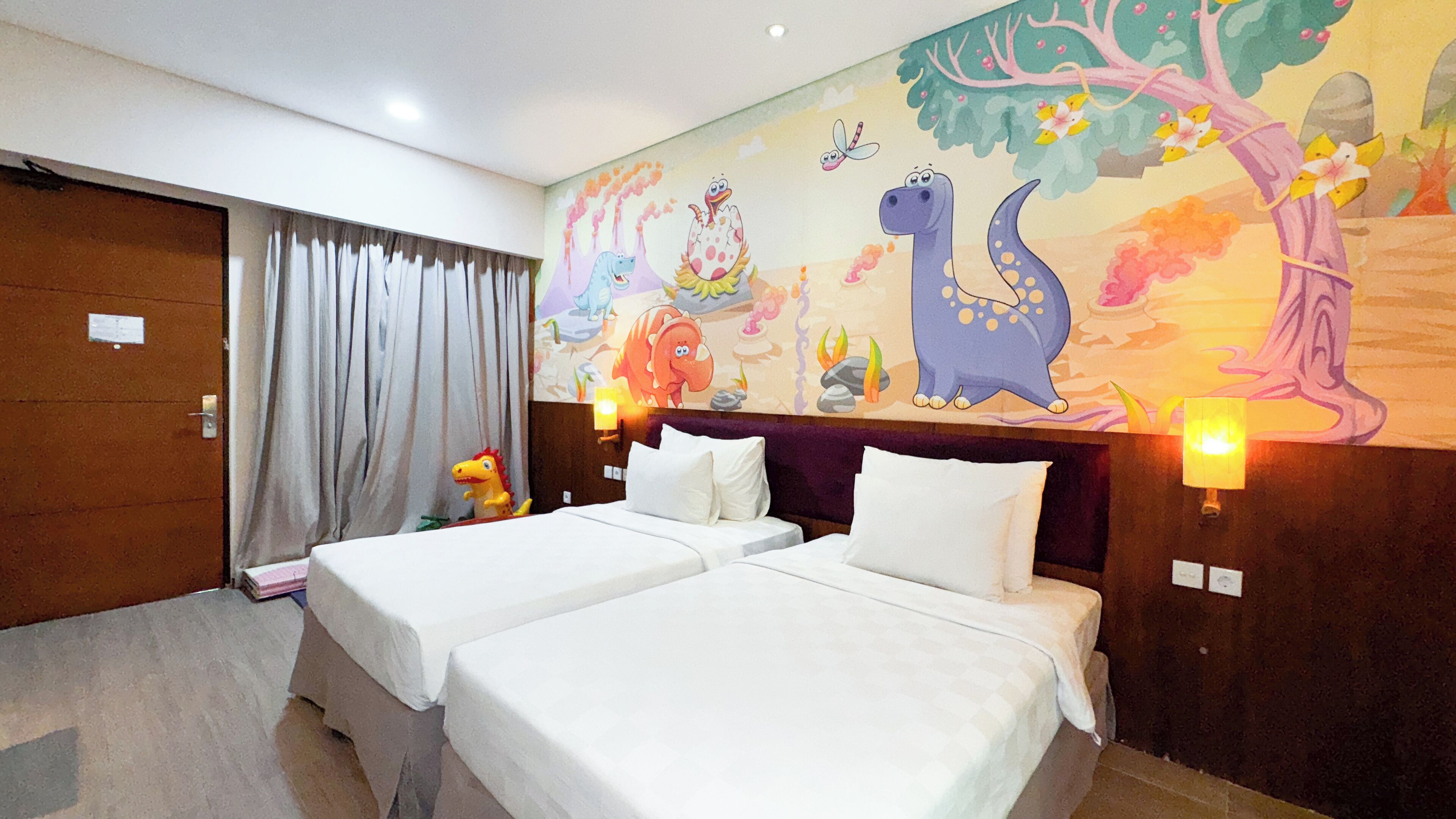Une chambre d’hôtel avec deux lits, une fresque murale et une fenêtre avec des rideaux.