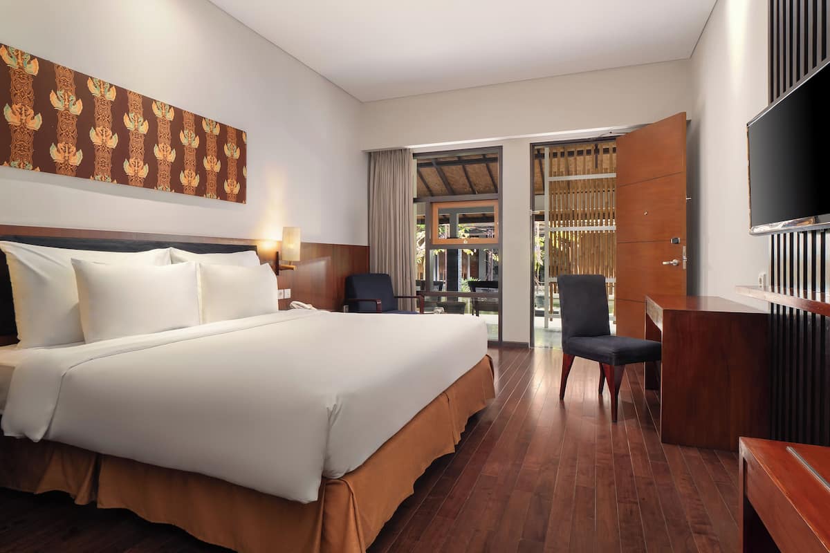 Ein Hotelzimmer mit einem großen Bett, einem Schreibtisch, einem Stuhl, einem Fernseher und Blick ins Freie.