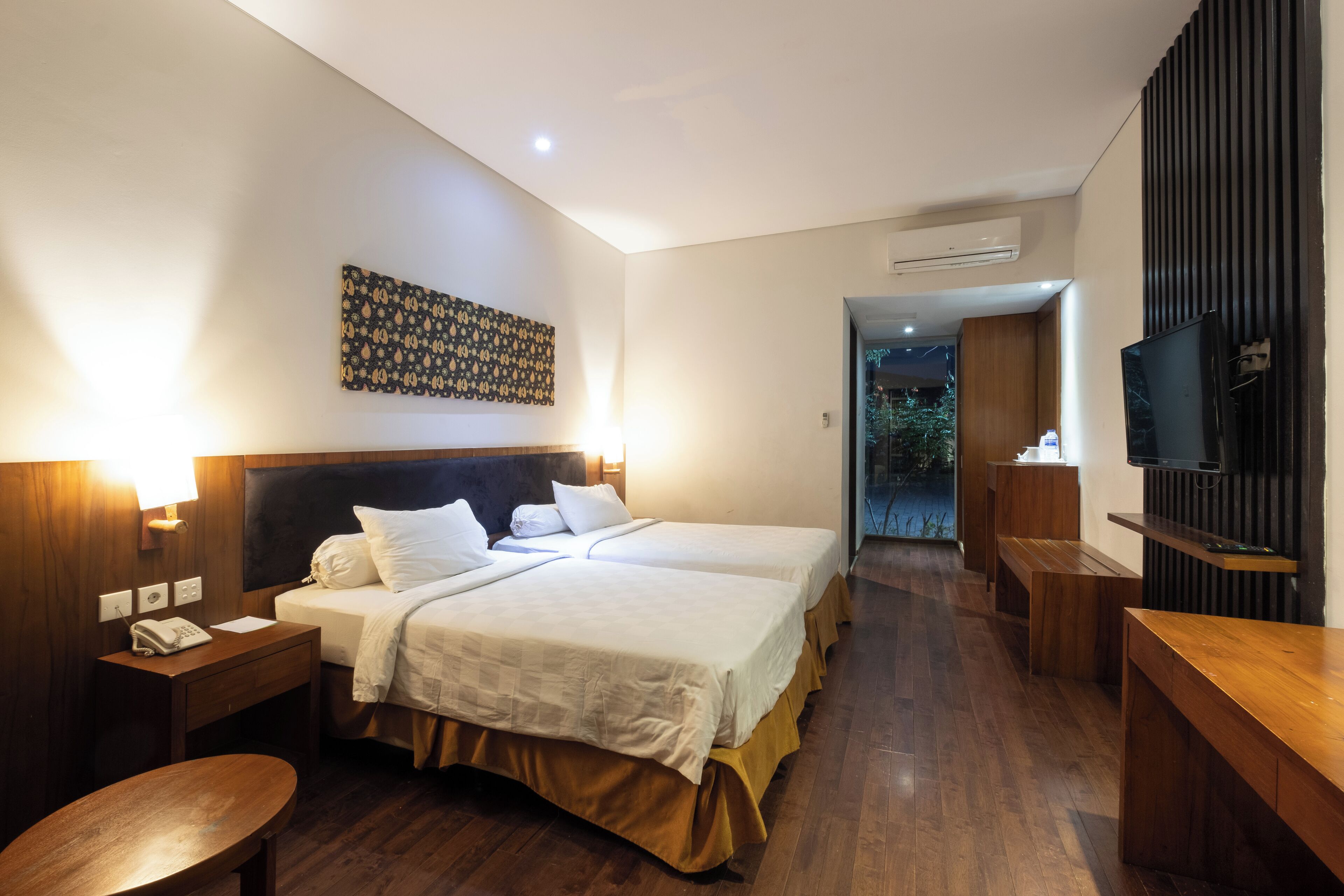 Ein Hotelzimmer mit zwei Betten, einem Holztisch, einem Fernseher und einer Klimaanlage.