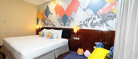 A hotel room with a bed, pillows, a nightstand, a lamp, a wall mural, a window, and a toy slide.