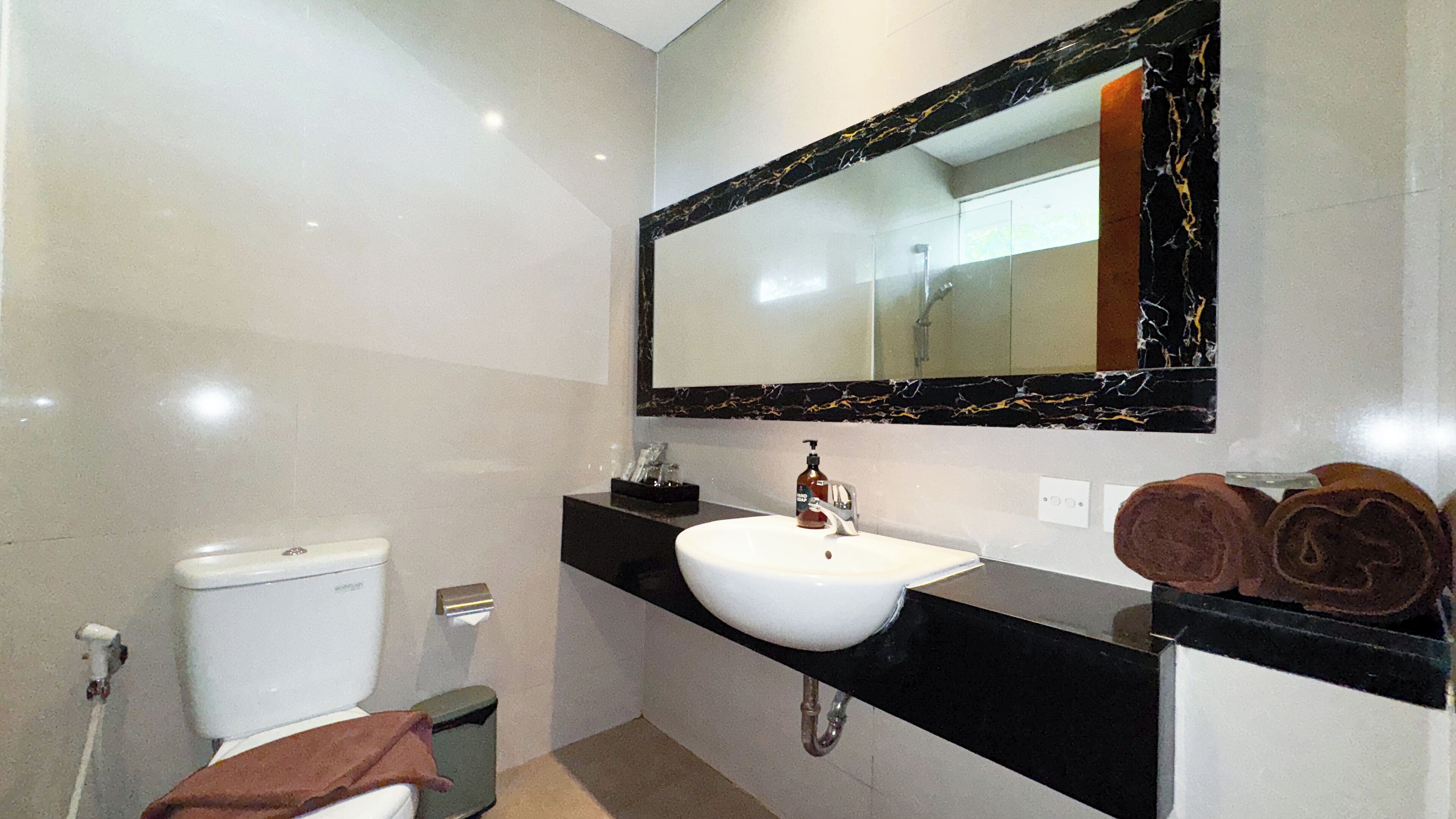 A modern bathroom with a white toilet, a black sink with a marble countertop, and a large mirror with a black frame.
