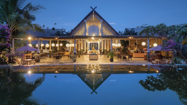 A modern hotel with a pool in the foreground, featuring outdoor seating and a well-lit entrance. - Rumah Kito Resort Hotel Jambi by WH (Jambi)