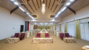A conference room with rows of tables and chairs, large windows with curtains, and a high ceiling with lighting fixtures. - Rumah Kito Resort Hotel Jambi by WH (Jambi)