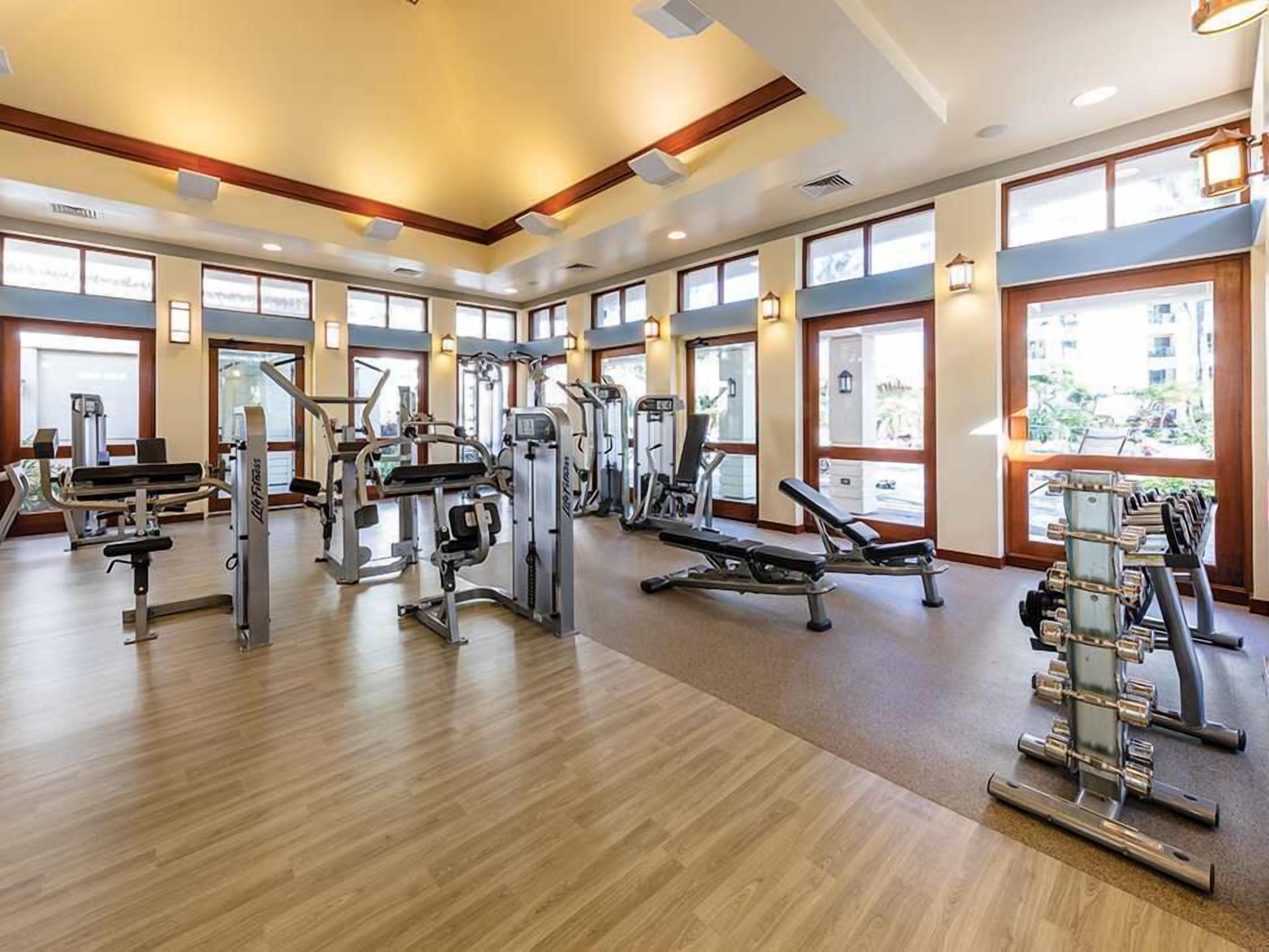 A gym with various exercise equipment, large windows, and a wooden floor.