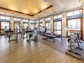 A gym with various exercise equipment, large windows, and a wooden floor.