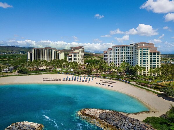Un hotel frente a la playa con varios edificios altos, una playa arenosa y un océano azul cristalino.