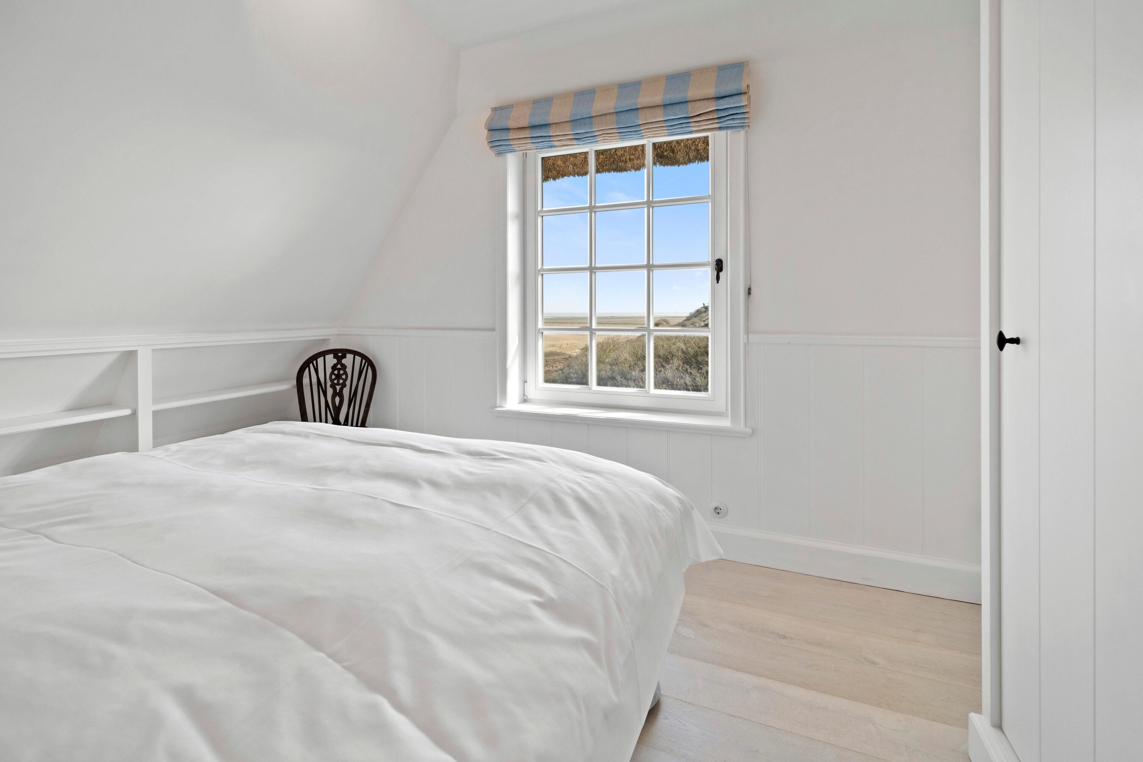 A bedroom with a large bed, a window with a view of the outdoors, and a chair against the wall.