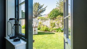 Blick durch ein Fenster auf einen Hinterhof mit Rasen, einem Holzzaun und einem Haus im Hintergrund.