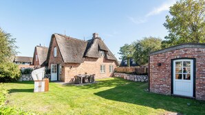 Ein traditionelles Backsteinhaus mit einem Reetdach, ein kleines Backstein-Nebengebäude und ein gepflegter Rasen.