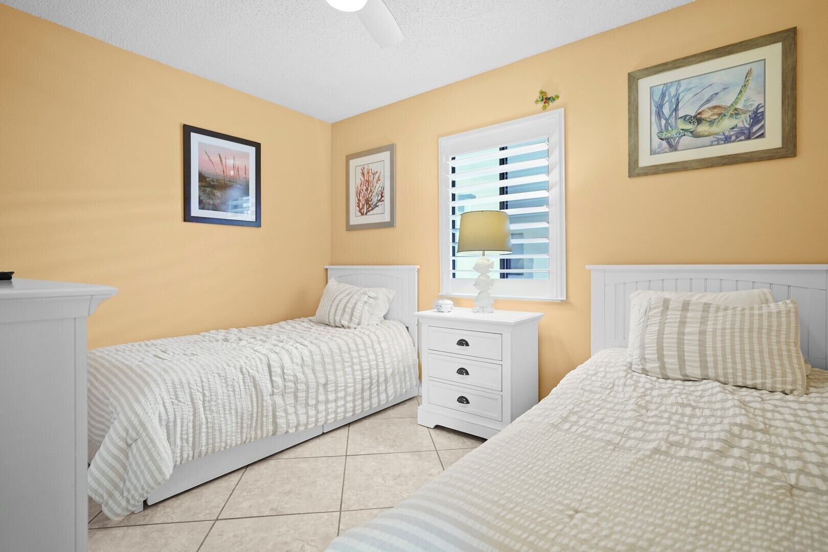 A bedroom with two single beds, a nightstand with a lamp, and a window with blinds.