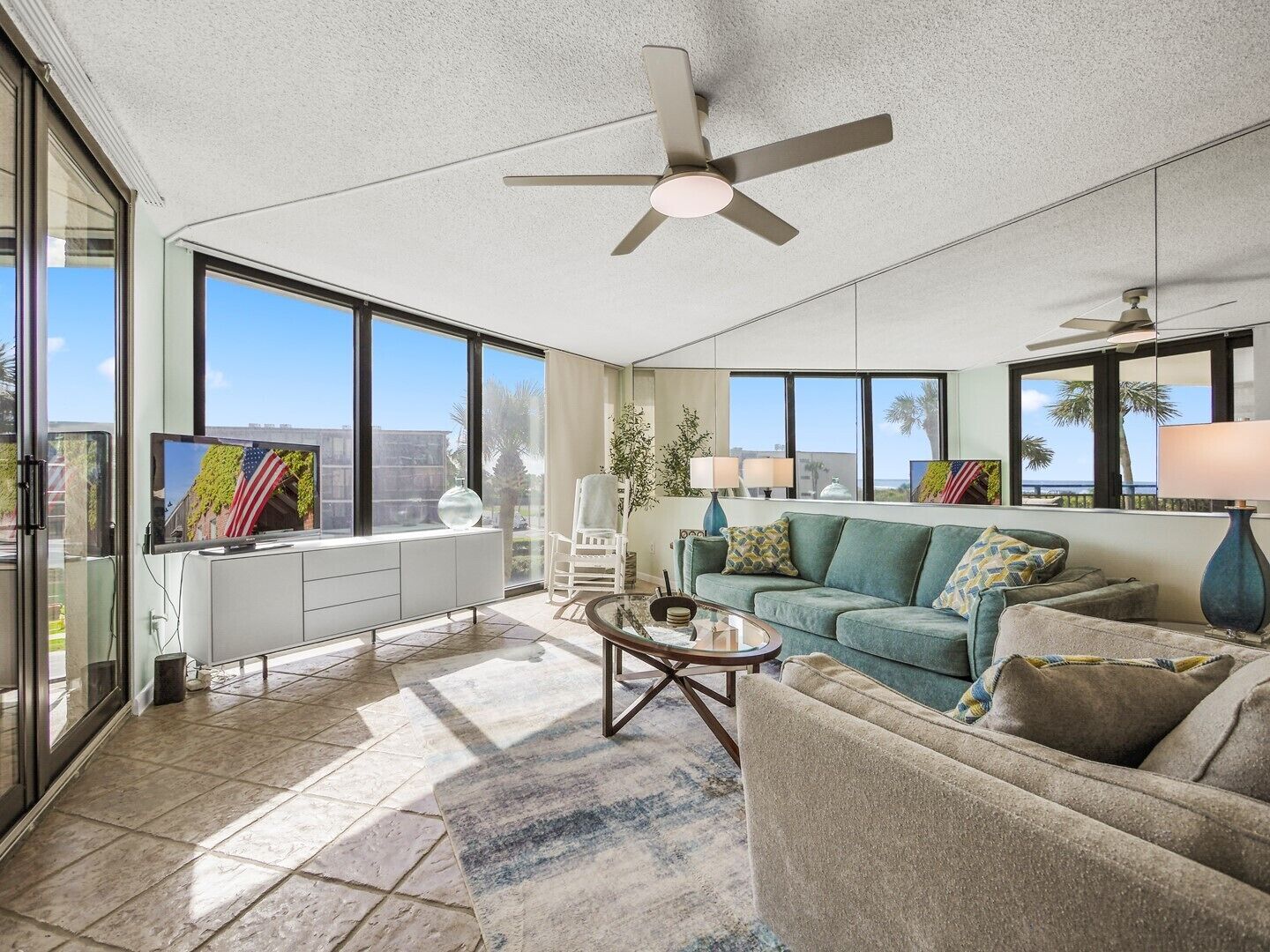 A spacious living room with large windows, a ceiling fan, and a view of the outdoors.