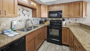 A kitchen with wooden cabinets, a microwave, an oven, a sink, and a clock on the wall. - Ocean Villas 19 -3 bed, 2 bath Ground floor unit just steps to the zero entry (St. Augustine Beach)