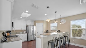 Una cocina moderna con armarios blancos, electrodomésticos de acero inoxidable y una isla central con taburetes de bar.