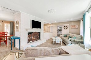A living room with a fireplace, a television, a sofa, and a dining area with a red chair and a blue table.