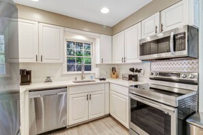 A modern kitchen with white cabinetry, stainless steel appliances, and a window providing natural light.