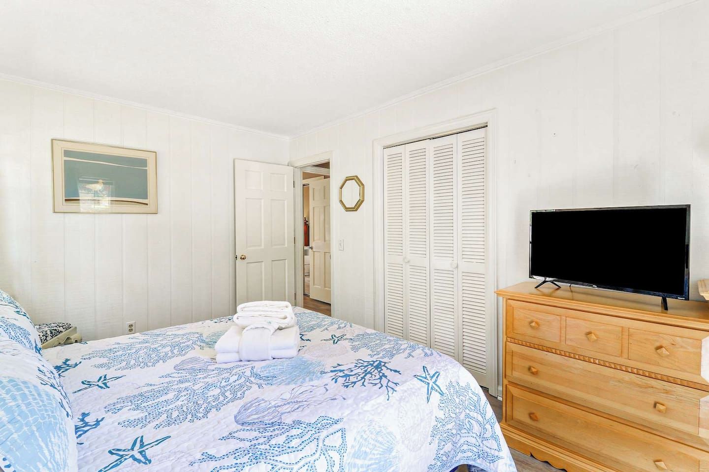 Un dormitorio con cama, cómoda, televisor y una puerta que da a otra habitación.