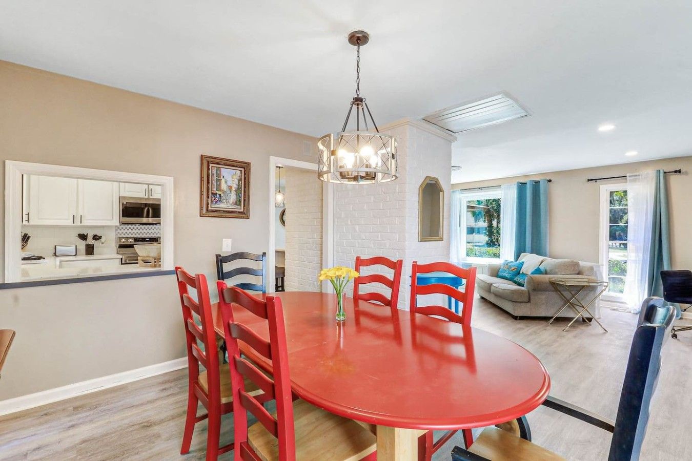 A modern kitchen with white cabinets, a dining table with red chairs, and a chandelier.
