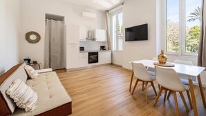 Ein modernes Wohnzimmer mit einer Couch, einem Esstisch mit Stühlen, einer Küchenzeile und einem an der Wand befestigten Fernseher.