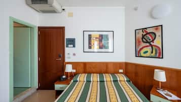 Une chambre d’hôtel comprenant un lit, une table de chevet, une lampe, un climatiseur fixé au mur et une porte.
