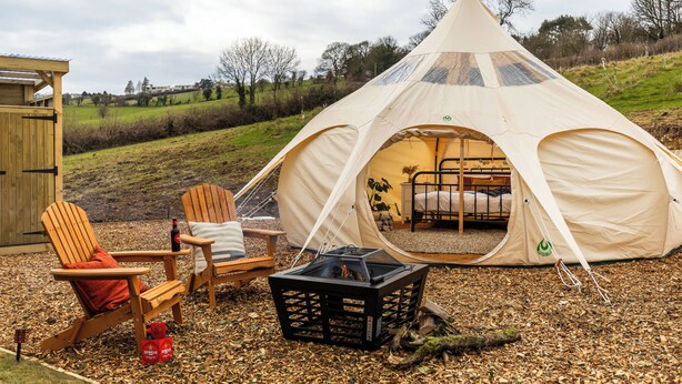 Een tent met een bed, twee houten stoelen, een tafel en een kist.